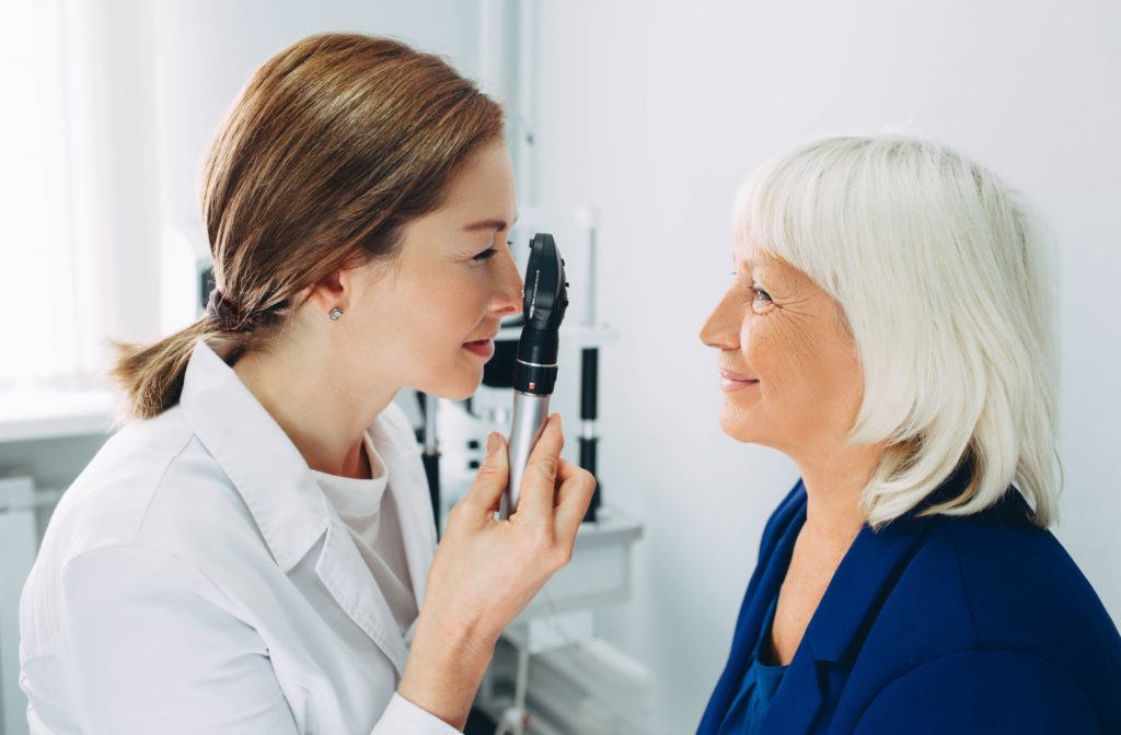 A young female optometrist examines a mature female patient's eye with a direct ophthalmoscope.