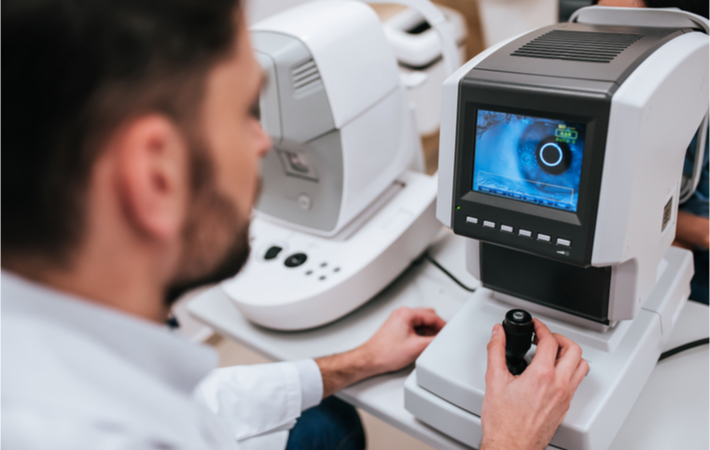 A young male optometrist examines the eye of a female patient with an autorefractor.