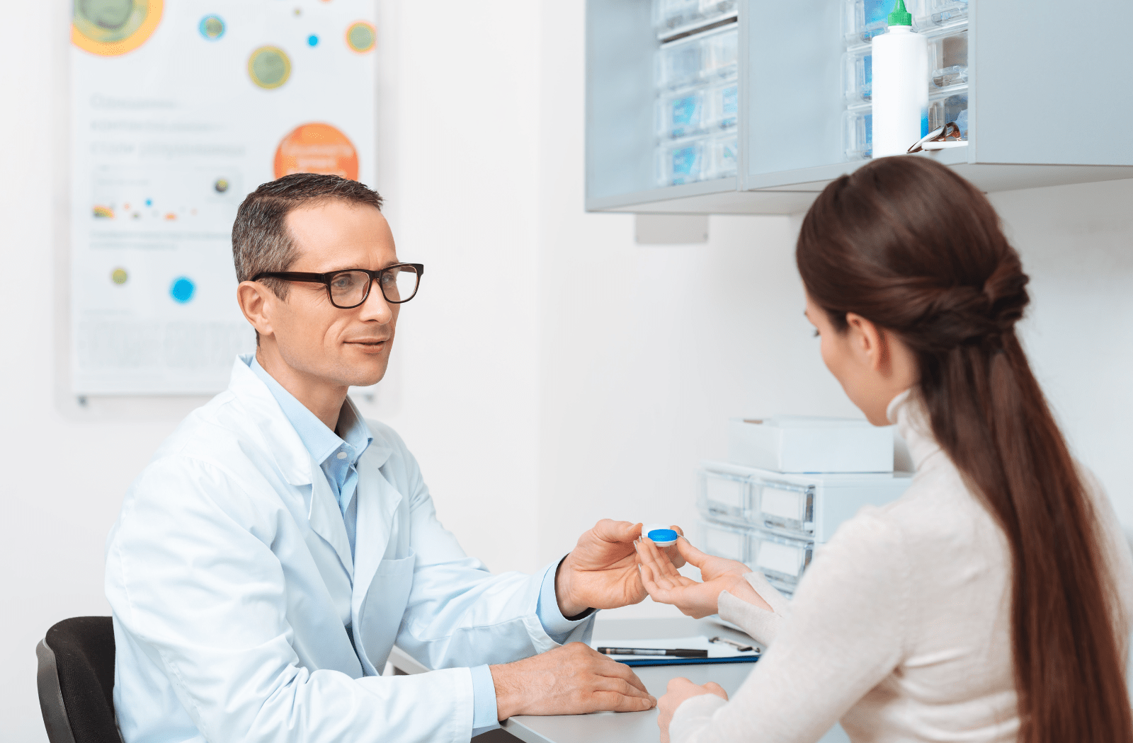 A male optometrist speaks to a female patient about wearing contact lenses while handing her a case