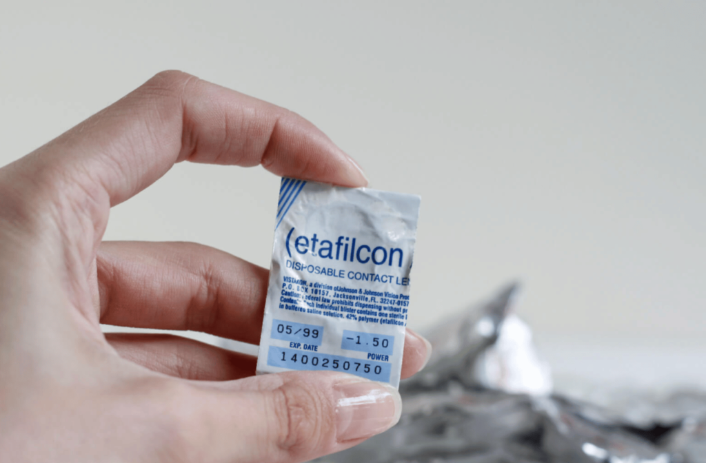 A hand is holding a pack of contact lens with expiration date on the label.