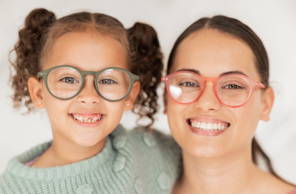 A mother and daughter smile together while they showcase their matching glasses after an eye exam