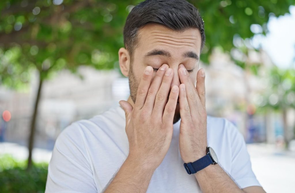 A young man standing outside rubbing his eyes, leading to the progression of keratoconus