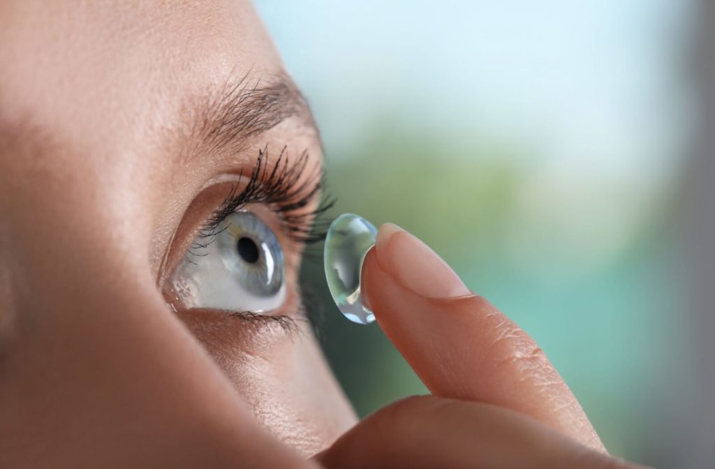 A close-up image of an adult carefully putting an ortho-k contact lens into their left eye.