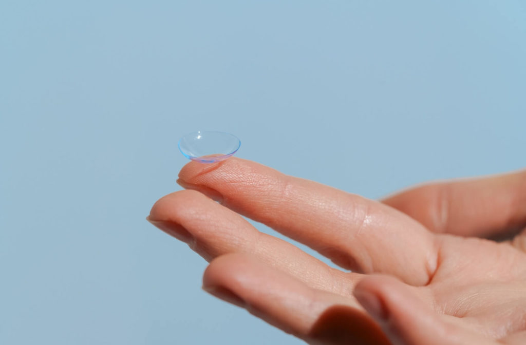 A close-up image of an ortho-k contact lens resting on the tip of a person's left index finger.