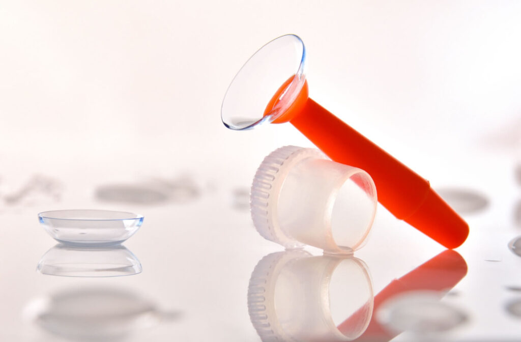 Close-up of a scleral contact lens on an orange applicator next to a white contact lens case, with another contact lens resting on the surface.