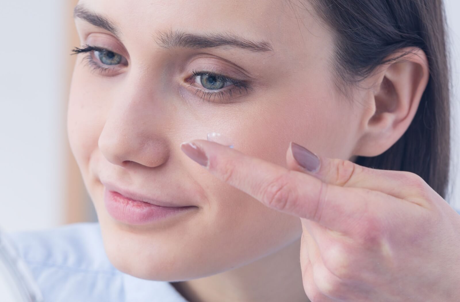 A young woman smiling and about to wear a contact lens on her fingertip.