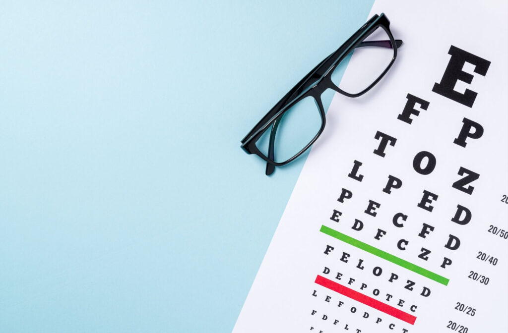 Black eyeglasses placed on a Snellen eye chart used for vision testing and eye exams.