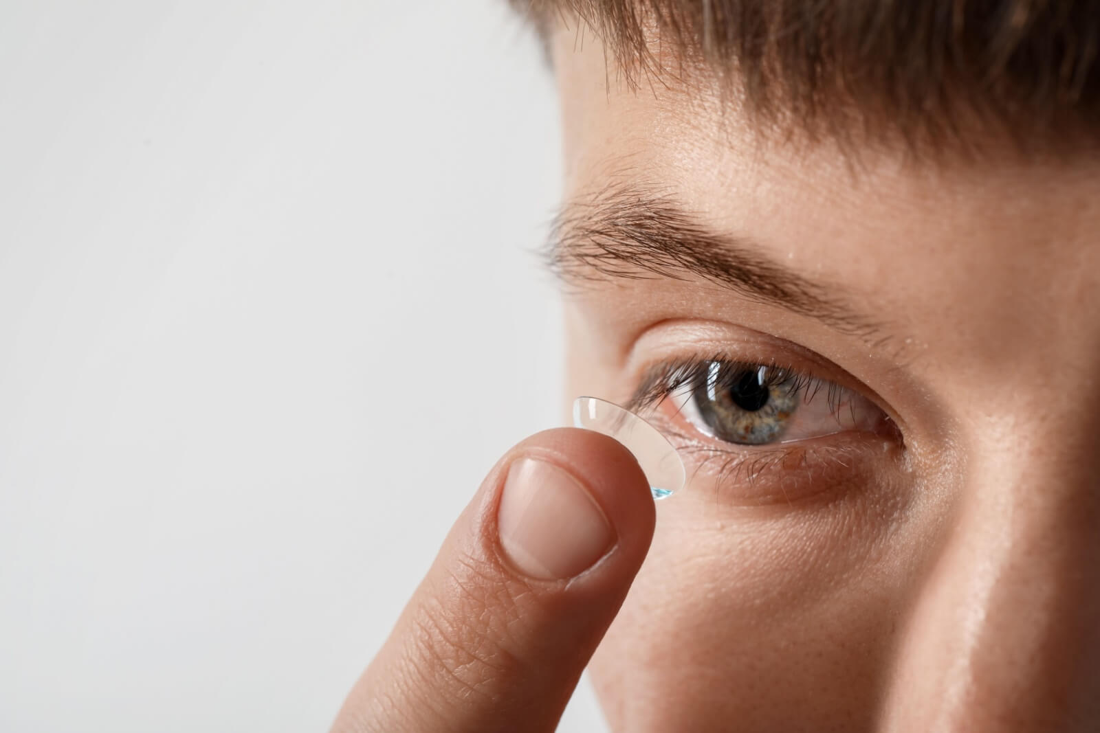 Man putting on contact lenses against light background, closeup.
